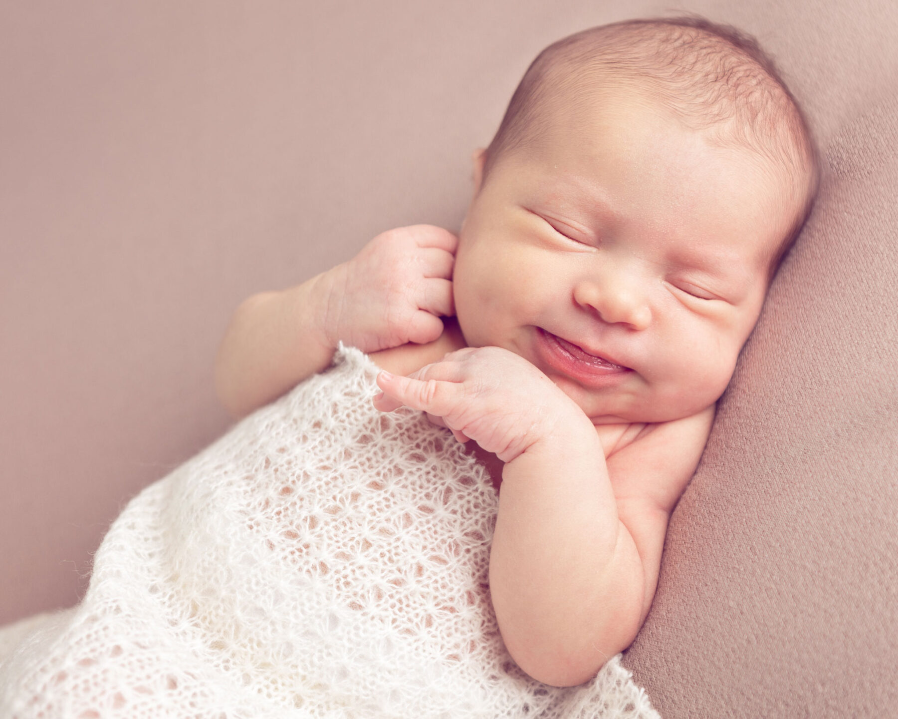 Newborn photography of a baby girl with a sweet smile in a white blanket