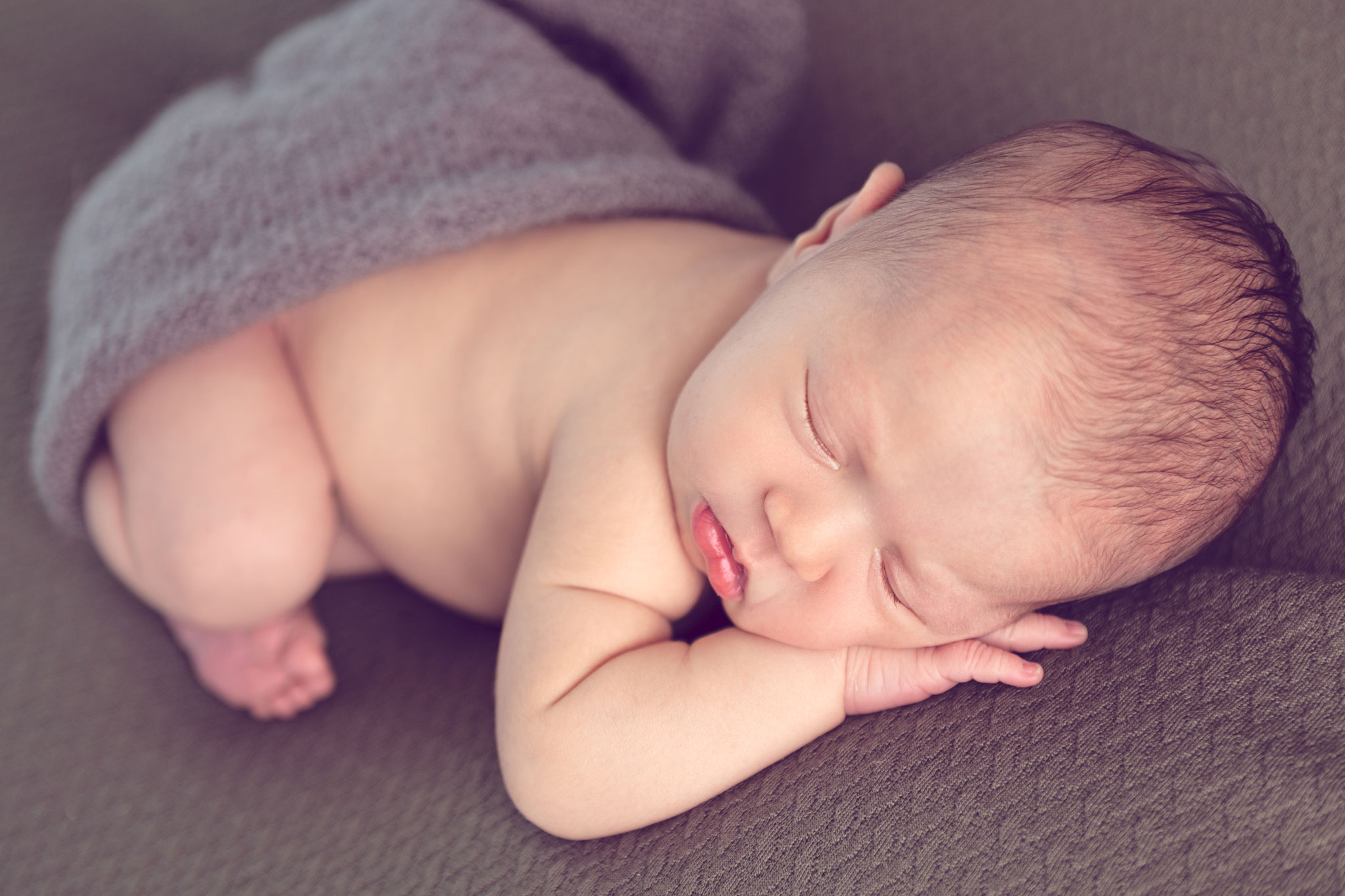 Newborn baby asleep on her stomach on a with her head resting on her hand.