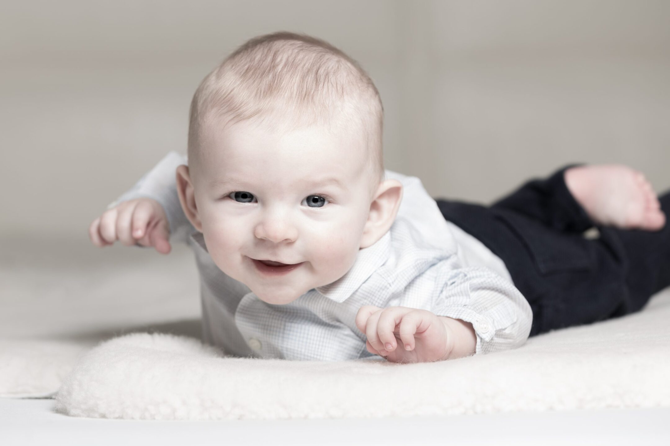 Newborn baby boy lying on his tummy and laughing wearing a shirt and trousers