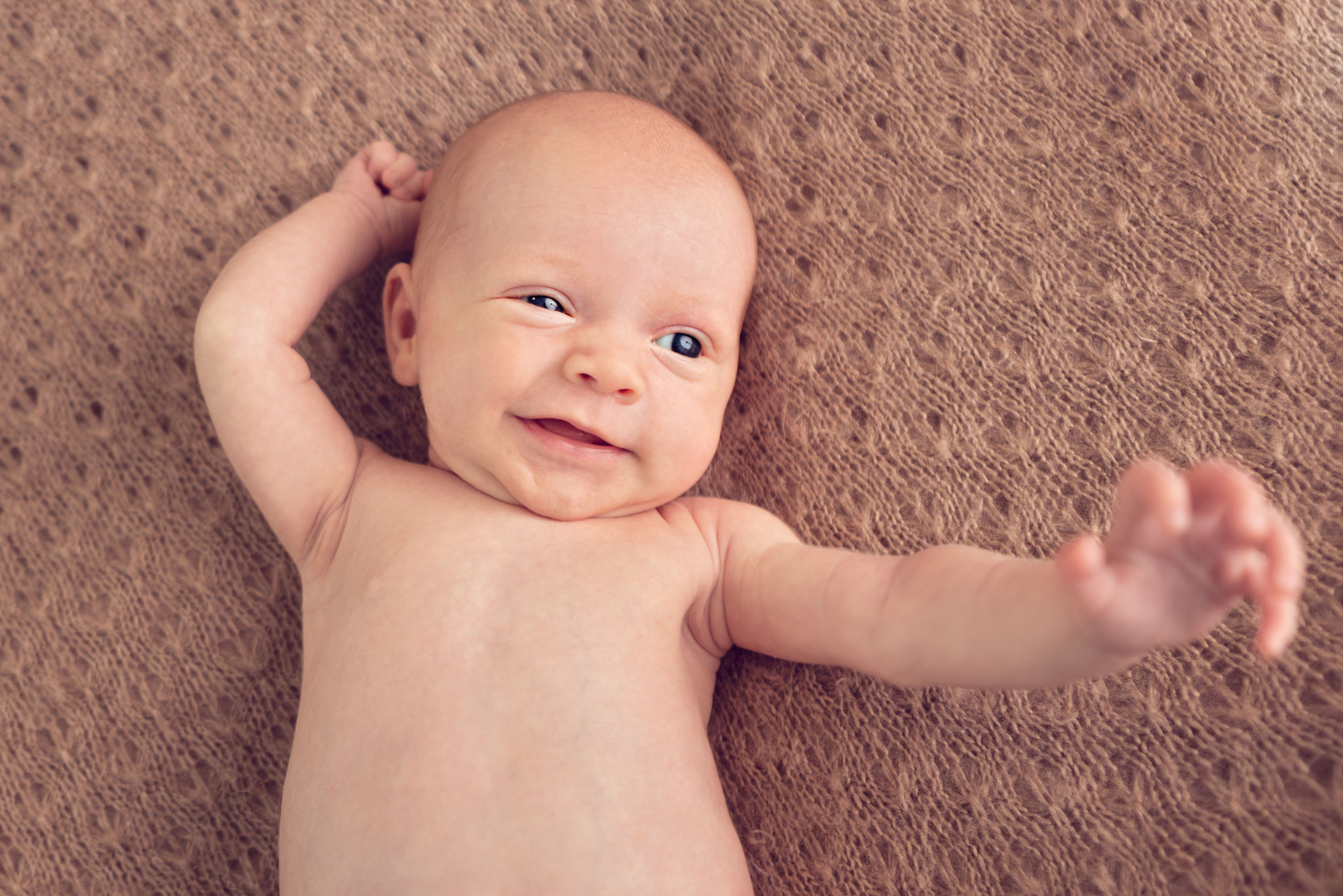 Happy baby smiling and stretching on a brown blanket.