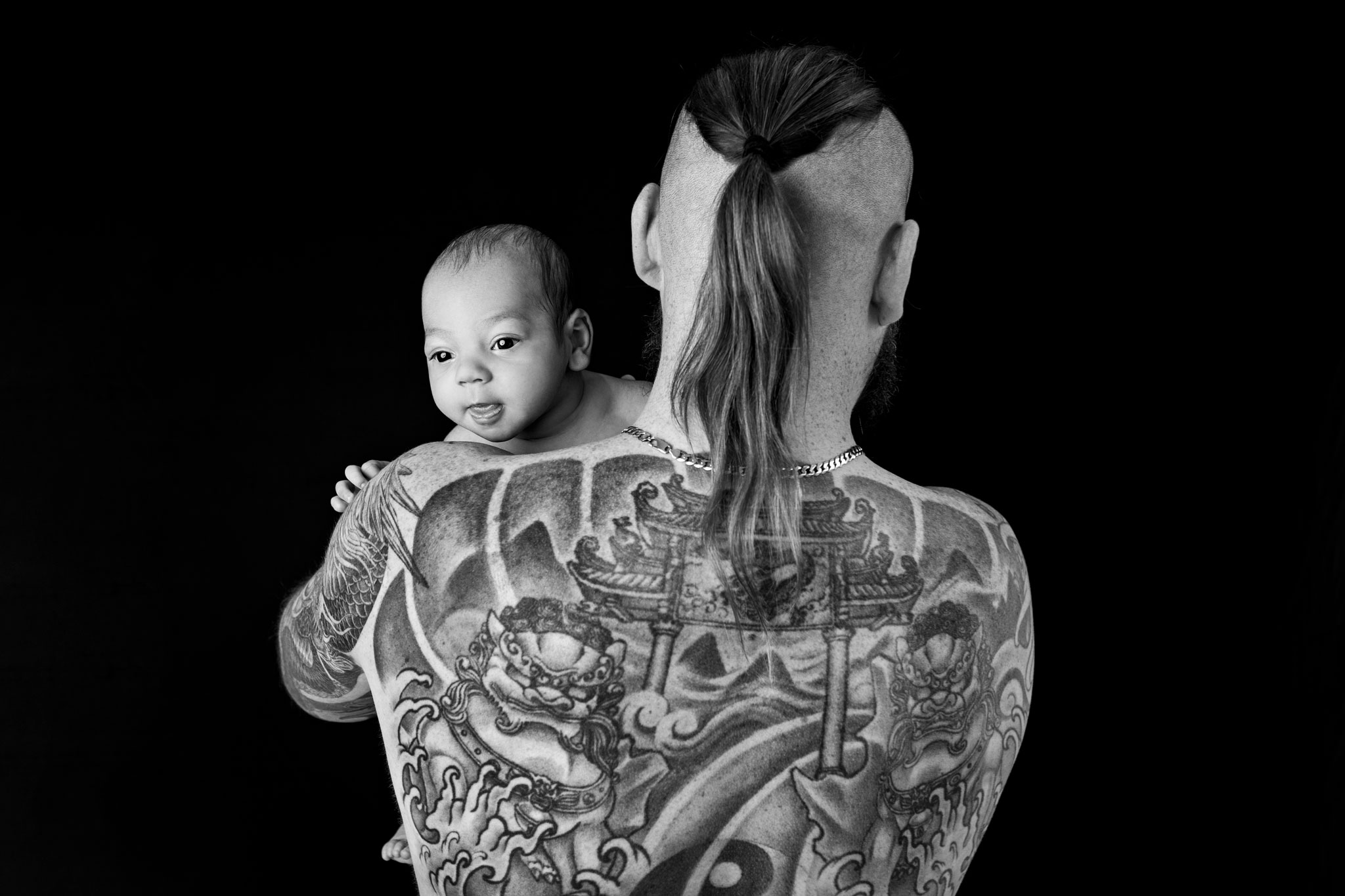 Baby looking over the shoulder of his father who has a tattooed back