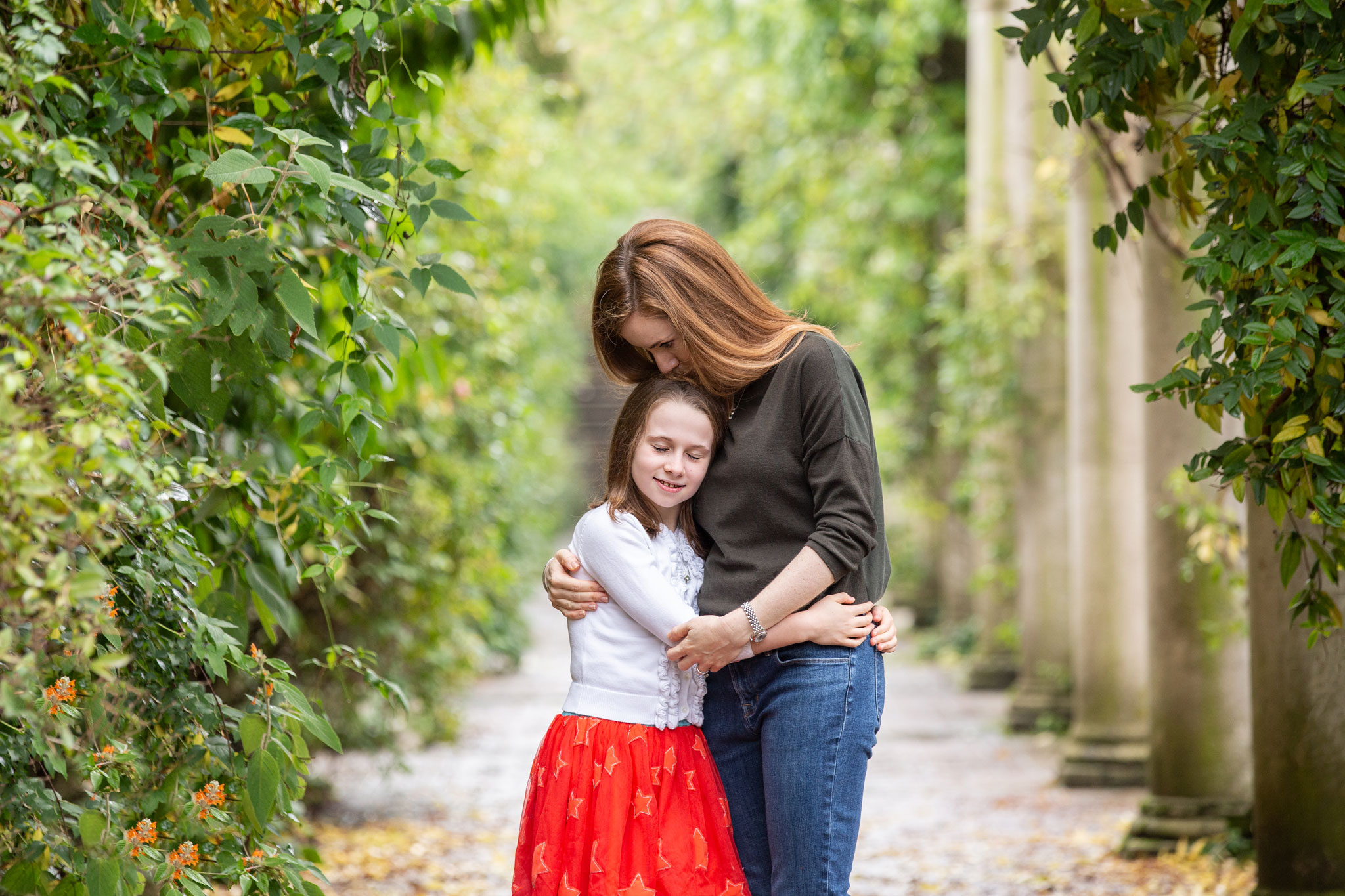 Mum kissing her daughter as they cuddle among leaves outdoors.