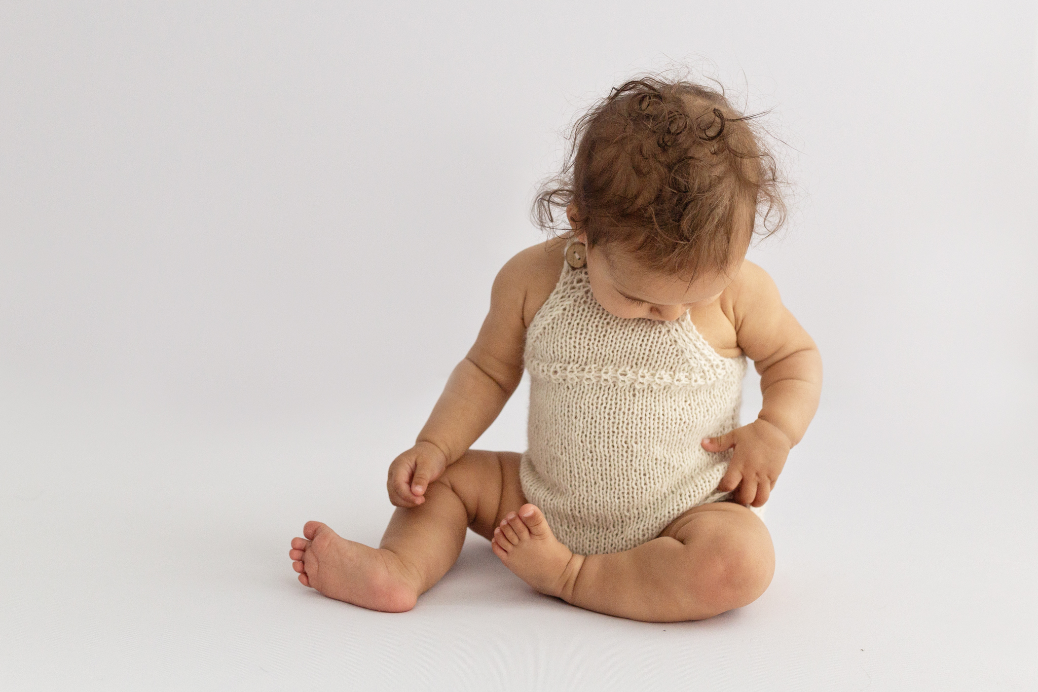 Baby girl with dark hair in knitted romper during sitter session