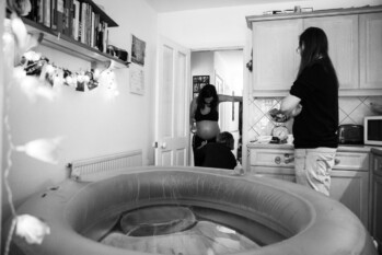 documentary photograph of a pregnant woman and her partner and midwife in front of a home birthing pool ready for labour