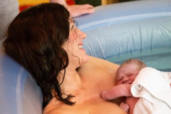 smiling mother as she holds her newborn baby on her chest minutes after giving birth to him in a home birth pool
