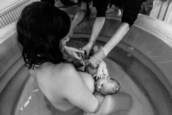dad cutting his newborn baby's umbilical cord while the mother hold the baby in a pool
