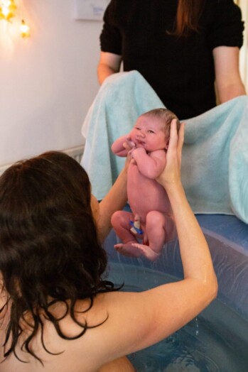 newborn baby being lifted out of a birth pool by his mother moments after being born